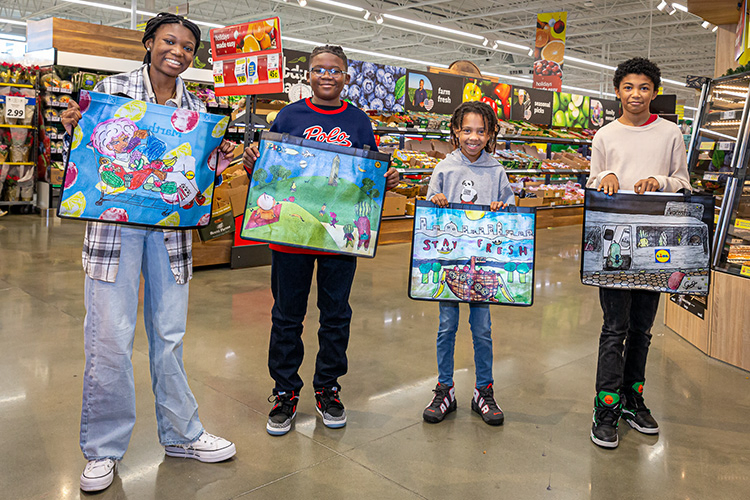 Akilah Daniels, Gabriel Trembath-Nicholson, Nyzear Allen and Zoe Amen students holding up shopping bags with their art printed on them inside Lidl (David Keith Photography)